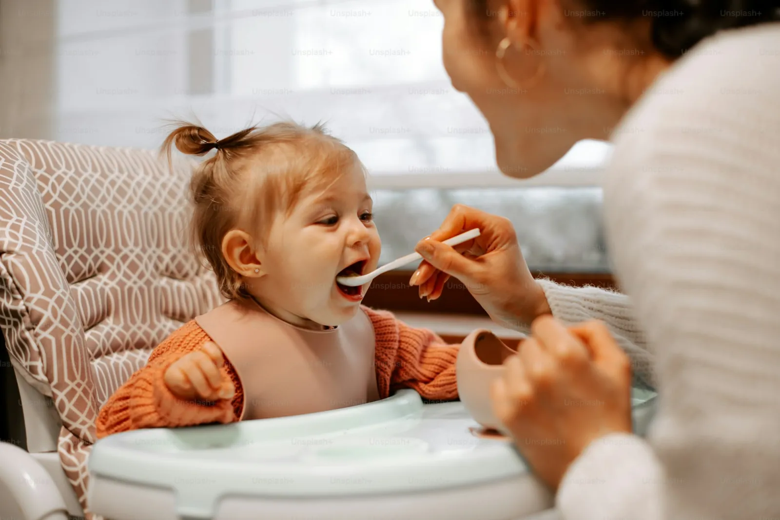 Mother spoon-feeding a toddler — shared utensils as a route of Streptococcus mutans transmission via saliva
